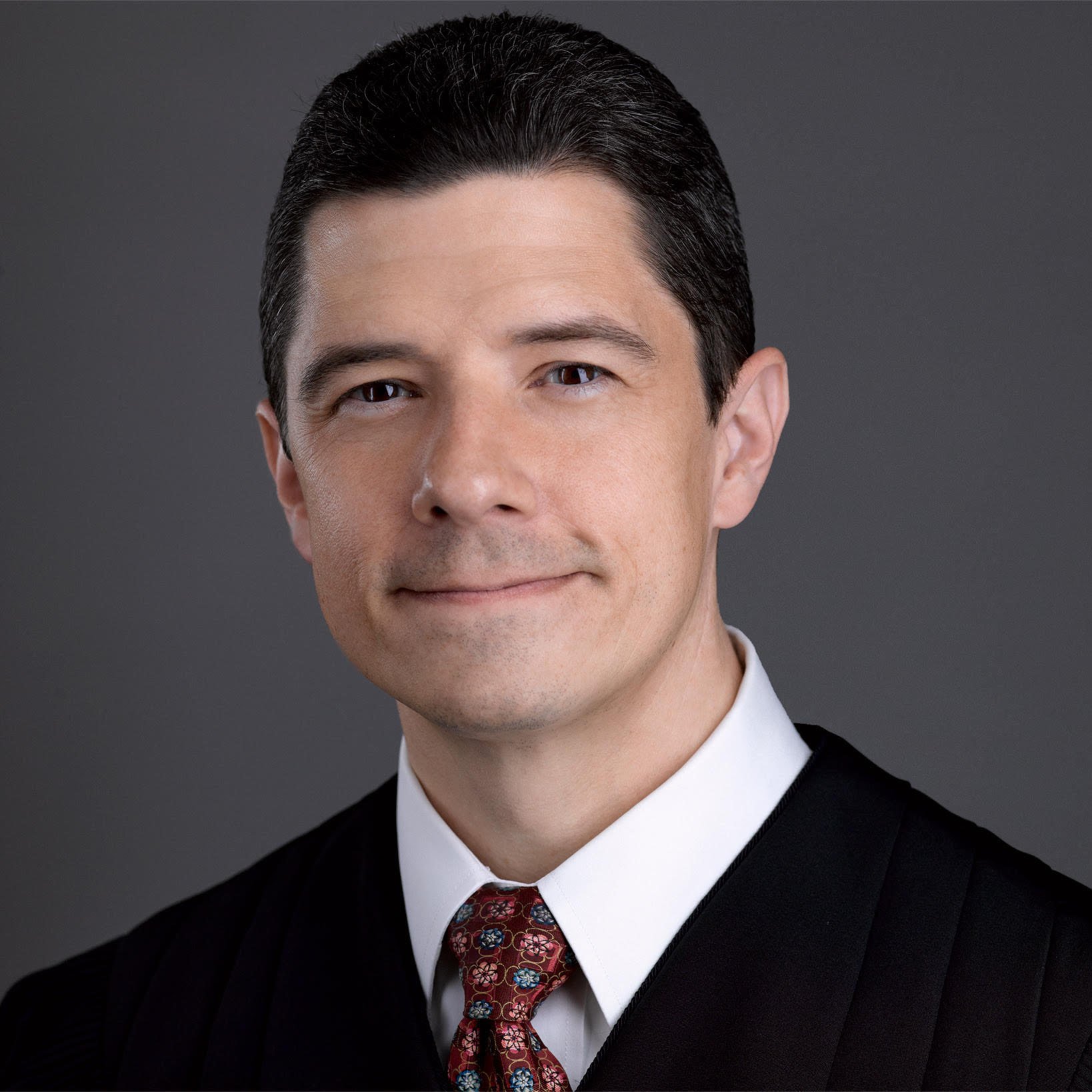 Justice Brett Busby wearing a suit and tie smiling and looking at the camera